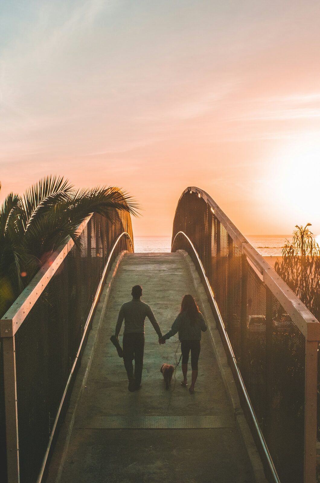 Een paar loopt hand in hand over een brug naar de zonsondergang